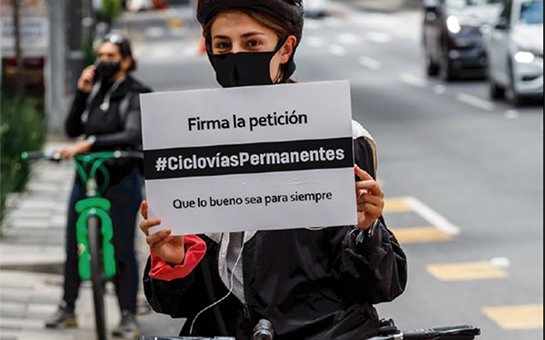 Chica en bicicleta mostrando una pancarta con la leyenda: Firma la petición | #CiclovíasPermanentes | Que lo bueno sea para siempre